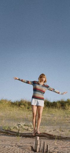 a woman standing on top of a wooden block in the sand with her arms outstretched