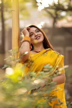 a woman in a yellow sari poses for a photo with her hand on the pole