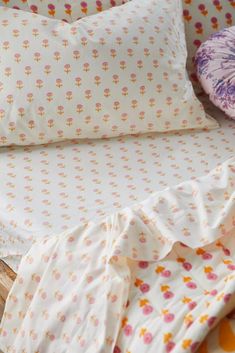 an unmade bed with white sheets and pink flowers on it, next to pillows