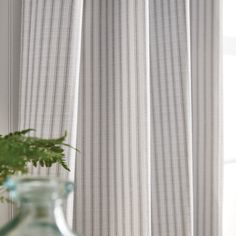 a vase filled with green plants next to a window covered in white sheers and curtains