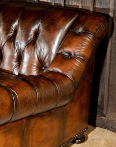 a brown leather couch sitting on top of a carpeted floor next to a wooden wall