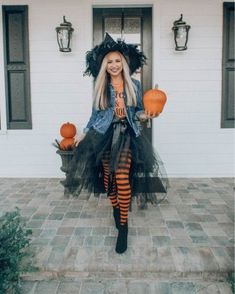 a woman dressed up as a witch standing in front of a house with pumpkins