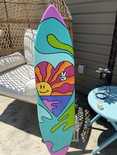 a colorful surfboard sitting on top of a patio next to a table and chair