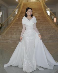 a woman in a white gown standing on the stairs with her arms around her waist