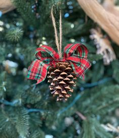 a pine cone ornament hanging from a christmas tree with red and green plaid ribbon