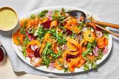 a salad with carrots, onions and lettuce on a plate next to dipping sauce