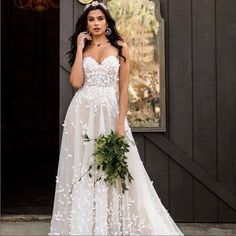 a woman in a white wedding dress holding a flower bouquet and posing for the camera