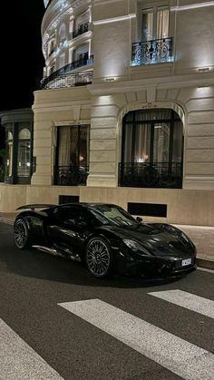 a black sports car is parked in front of a building at night with its lights on