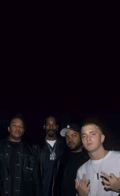 four men standing together in front of a dark background with one man holding his hands up