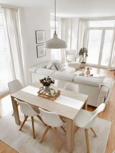 a white living room and dining area with wood flooring, couches, table and chairs