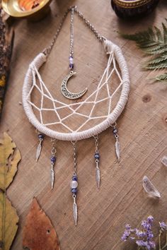 a white dream catcher sitting on top of a wooden table next to leaves and flowers