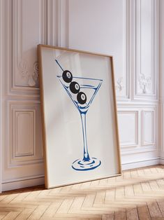 an art print with two olives in a martini glass on the floor next to a white wall