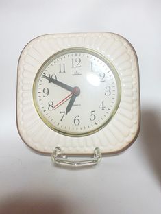 a white clock sitting on top of a table next to a banana peel holder with two hands