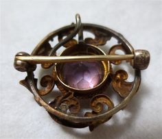 Antique Art Nouveau Gold and Amethyst Brooch or Pendant - 14 K Gold A swirled contrivance of Art Nouveau Design.. A small little jewel of a Pin.. of 14K Gold and discretely sized at 2 cm wide...like a delicate little button. Bezel set in the center, a large Amethyst rose-cut stone. The table is in very fine shape- with no scratches or wear. On the reverse, a simple , old fashioned C Clasp secures.. and a graceful sweep of wire forms the hidden means to string along a chain, that the piece might Round Gold Brooch With Gemstone, Round Gold Brooches With Gemstone, Purple Brooch Jewelry Gift, Gold Gemstone Round Brooch, Gold Gemstone Round Brooches, Purple Amethyst Brooch As A Gift, Amethyst Brooch Jewelry Gift, Purple Gemstone Brooches For Weddings, Purple Amethyst Brooches For Wedding