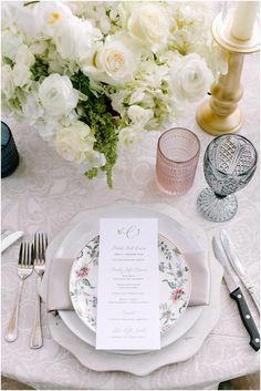 the table is set with white flowers and silverware