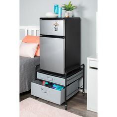 a silver refrigerator freezer sitting on top of a metal drawer next to a bed