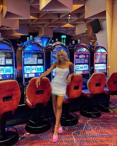 a woman standing in front of slot machines at a casino or gambling hall with red chairs