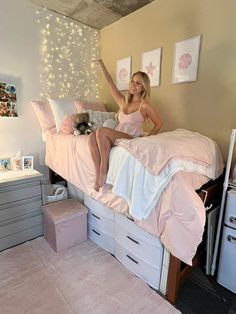 a woman sitting on top of a bed in a room with pink sheets and pillows