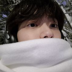 a young man with headphones covering his face and wearing a white scarf around his neck