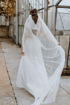 a woman in a white dress and veil is walking down the street with her back to the camera