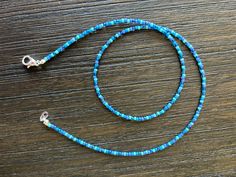 a blue beaded lanyard on a wooden table with a metal hook in the middle