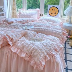 a bed with pink ruffled sheets and pillows in front of a large window that has a smiley face drawn on it