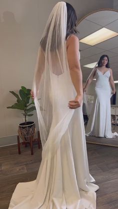 a woman in a wedding dress looking at her reflection in the mirror while wearing a veil