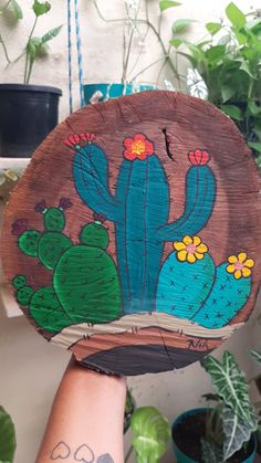 a person holding up a piece of wood with cactus designs on it and flowers in the background