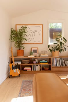 a living room filled with furniture and a guitar on top of a wooden shelf next to a window