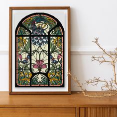 an ornate stained glass window in a wooden frame next to a vase with dried flowers