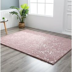 a pink rug in a white room with wooden flooring and potted plant on the far side