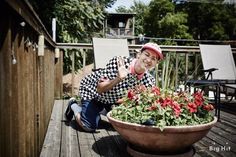 a man kneeling down next to a large pot filled with flowers on top of a wooden deck