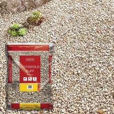 a red and yellow package sitting on top of a pile of gravel next to a plant