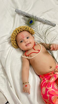 a baby wearing a headdress laying on top of a white bed next to a feather