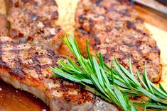 two pieces of meat on a cutting board with some green garnish around it