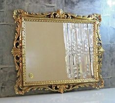 a gold framed mirror sitting on top of a white counter next to a brick wall