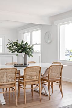 a dining room table with four chairs and a plant in a vase on top of it