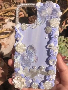 a hand holding up a phone case with flowers and pearls on the back in front of it