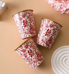 three red and white cups sitting on top of a table next to a pink flower