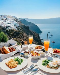 an outdoor table with food and drinks overlooking the ocean on a sunny day in greece