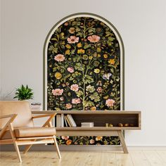 a chair sitting next to a book shelf in front of a wall with flowers on it