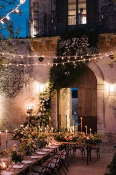 an outdoor dining area with candles and flowers on the table, surrounded by greenery