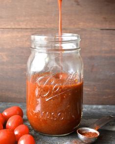 a glass jar filled with sauce next to some tomatoes and a spoon on a table