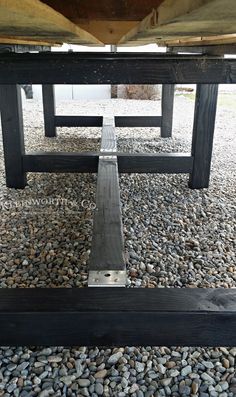 a wooden table sitting on top of a gravel covered ground next to a metal pole