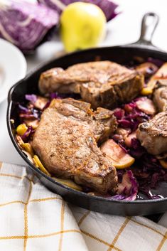 a skillet filled with meat and vegetables on top of a table next to an apple