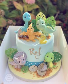 a birthday cake decorated with dinosaurs and sea creatures on a white box in front of pink flowers