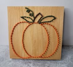 two pumpkins made out of beads on a wooden board