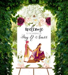 a welcome sign with two women holding hands in front of flowers and greenery on an easel