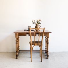 a wooden table with two chairs and a vase on top of it next to a white wall