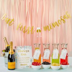 a table topped with bottles of wine and bowls filled with fruit next to a banner